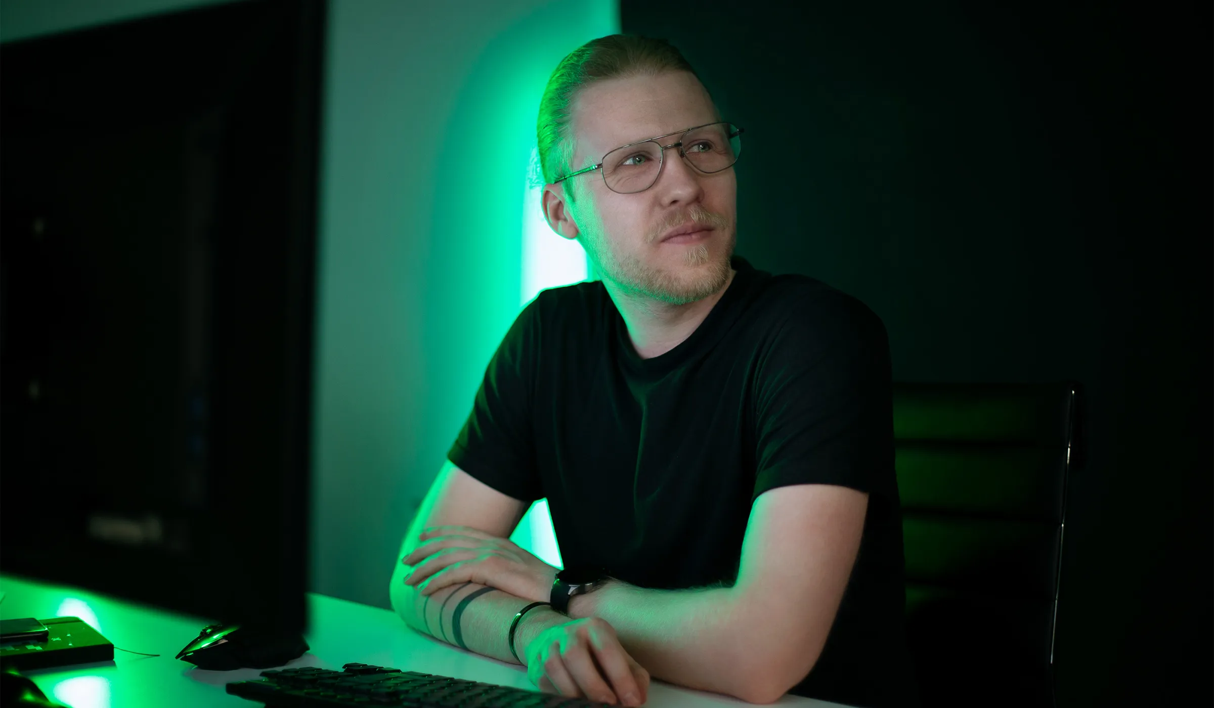 Blonde Person mit brille sitzt in Büro mit grüner Hintergrundbeleuchtung